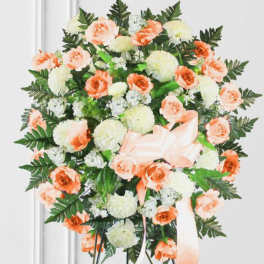 Peach and white floral standing wreath with a ribbon bow