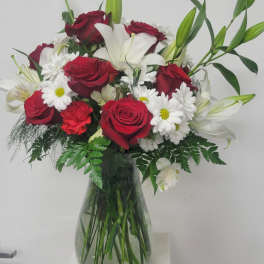Bouquet of red roses, white lilies, and daisies in a glass vase