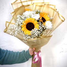 Bouquet of sunflowers and white daisies wrapped in gold paper with a pink ribbon