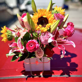 Bright bouquet of pink roses, lilies, and sunflowers in a white box