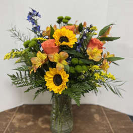 Mixed bouquet with sunflowers, orange roses, and blue flowers in a glass vase