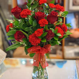 Red roses and carnations in a clear glass vase with a red ribbon