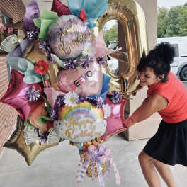 Woman holding a large birthday balloon bouquet with flowers and money accents