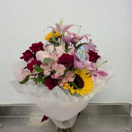 Mixed bouquet of roses, lilies, and a sunflower in a glass vase