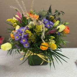 Mixed bouquet of purple daisies and orange blooms in a green container