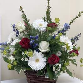 Basket arrangement with red and white roses, white daisies, and blue flowers