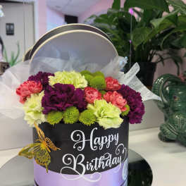 Birthday flower arrangement in a round gift box with pink, purple, and green blooms