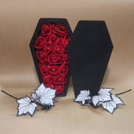 Black coffin-shaped box filled with red roses and white spiderweb leaves