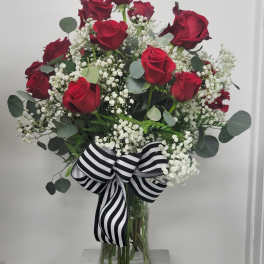 Red roses in a glass vase with white baby's breath and a striped ribbon