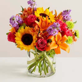 Bouquet of sunflowers, roses, lilies, and purple blooms in a glass vase