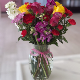 Mixed bouquet of roses and carnations in a glass vase with a pink ribbon