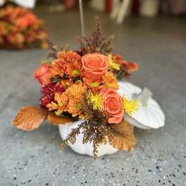 Orange and yellow floral arrangement in a white pumpkin container