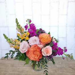 Bouquet of peach and blush roses with purple flowers in a glass vase