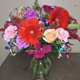 Colorful bouquet of gerbera daisies, roses, and carnations in a glass vase
