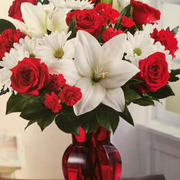 Red roses, white lilies, and white daisies in a red glass vase