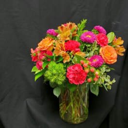 Mixed bouquet of orange, pink, and red flowers in a glass vase