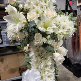 White roses, lilies, and chrysanthemums arranged in a tall spray with a white ribbon.