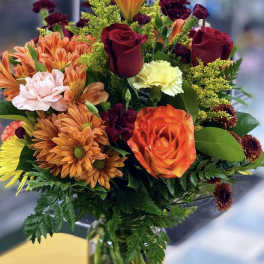 Mixed bouquet of orange, red, and pink flowers in a clear glass vase