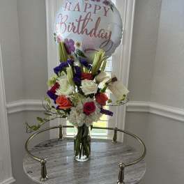 Birthday balloon above a mixed flower arrangement in a glass vase