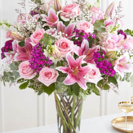 Tall glass vase filled with pink lilies, pink roses, and white and purple filler flowers