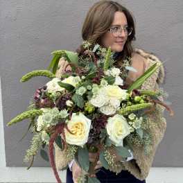 Woman holding a large bouquet of white and pale yellow roses with green accents