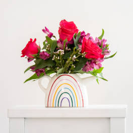 Pink roses and purple flowers in a rainbow pitcher vase