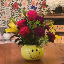 Mixed bouquet in a yellow smiley-face vase with roses and lilies