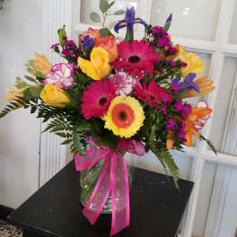 Bright mixed bouquet in a glass vase with a pink ribbon
