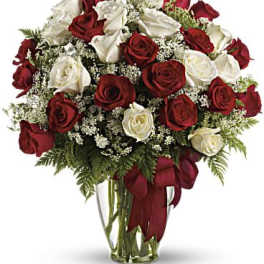 Red and white roses in a clear glass vase with a red ribbon