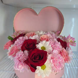 Pink heart-shaped box filled with red and pink roses and daisies