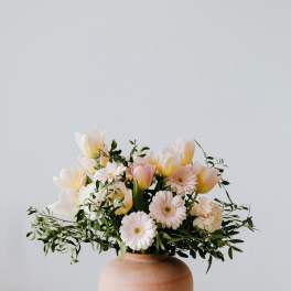 Pastel bouquet of tulips and daisies in a terracotta vase
