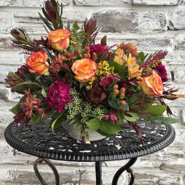 Mixed bouquet of orange roses and magenta flowers in a white vase