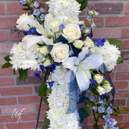 White floral standing spray with blue accents on an easel