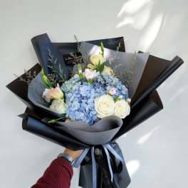 Bouquet of blue hydrangeas and white roses wrapped in black paper