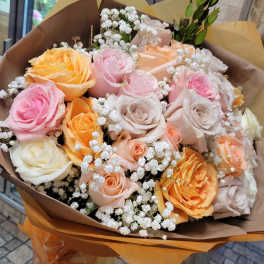 Handheld bouquet of pink, peach, and cream roses wrapped in brown paper