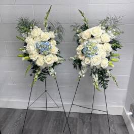 Two white rose and blue hydrangea standing floral sprays on black easels