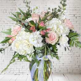 Large bouquet of pink and white flowers in a glass vase with a ribbon