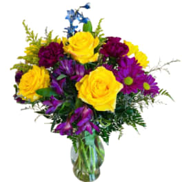 Bouquet of yellow roses and purple flowers in a glass vase