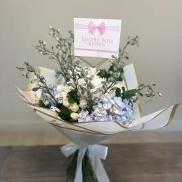 Bouquet of pale blue and white flowers wrapped in white paper with a ribbon