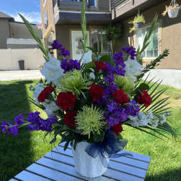 Large mixed floral arrangement in a white vase with purple, red, and white blooms