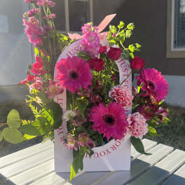 Pink gerbera daisies and roses arranged in a white gift bag