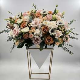Large pastel floral arrangement in a white container on a gold stand