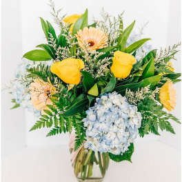 Bouquet of yellow roses, gerbera daisies, and blue hydrangea in a glass vase