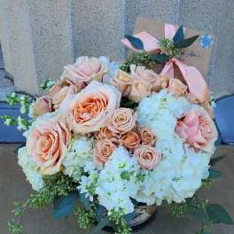 Low arrangement of peach roses and white hydrangeas in a glass vase with a card tied by a ribbon