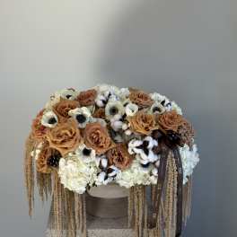 Large arrangement of tan roses, white blooms, and cotton stems in a round container