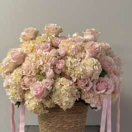 Pink roses and hydrangeas in a woven basket with ribbon tails