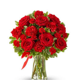 Red roses and carnations in a clear glass vase with a red ribbon