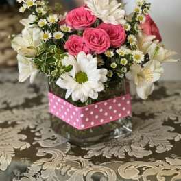 Pink roses and white daisies arranged in a glass vase with a pink polka-dot wrap