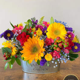 Low galvanized tin arrangement of bright sunflowers, red roses, and mixed colorful blooms