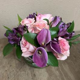 Pink roses and purple calla lilies in a glass bowl vase